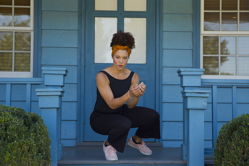 A woman crouches down cupping her hands on a blue porch